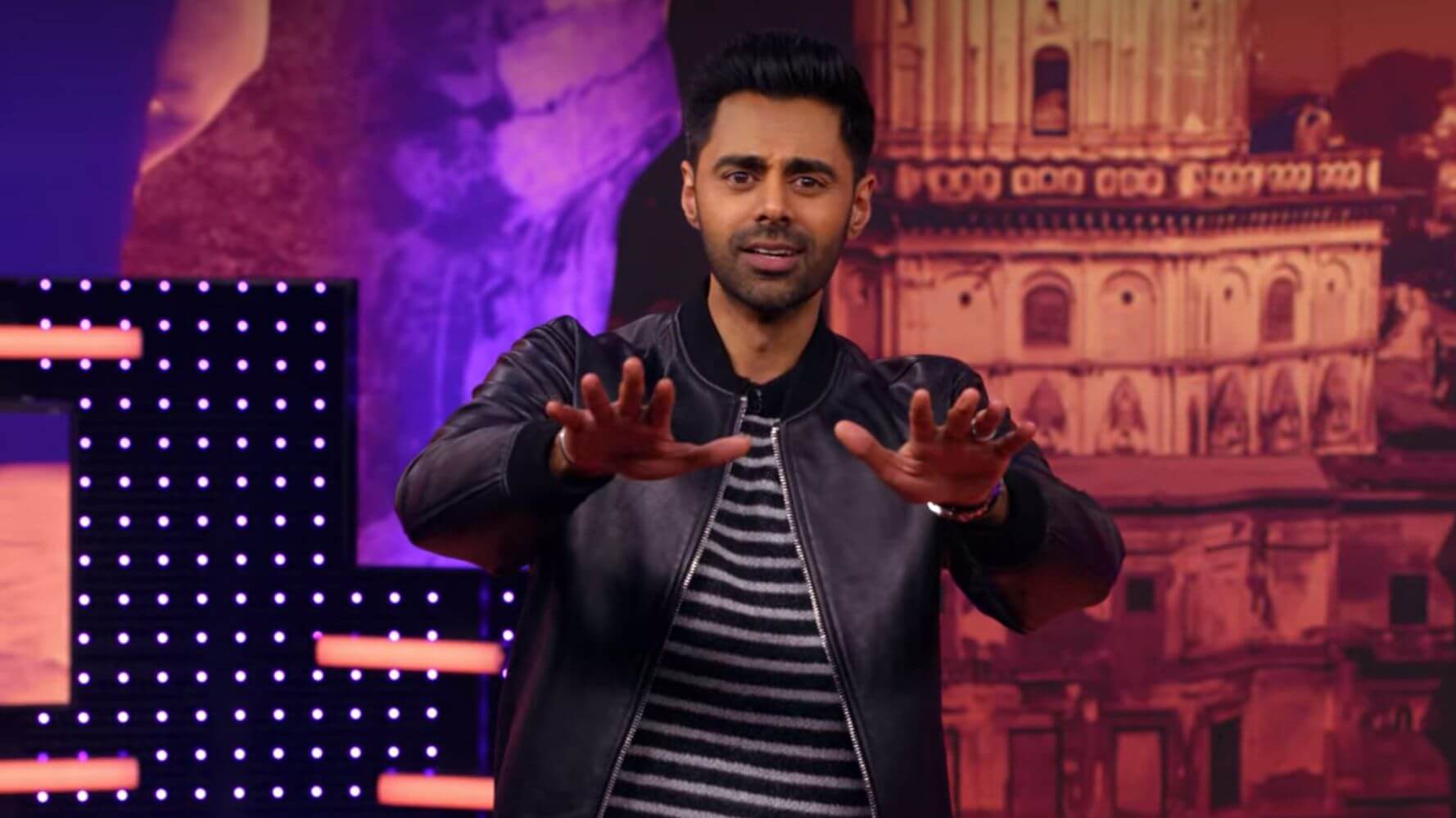 Hasan Minhaj dengan bomber jacket hitam dan atasan garis-garis